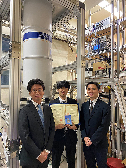 小寺哲夫准教授（右）、二谷時緒さん（中央）、米田淳特任准教授（左）。<br>奥は実験で用いた希釈冷凍機と測定系。