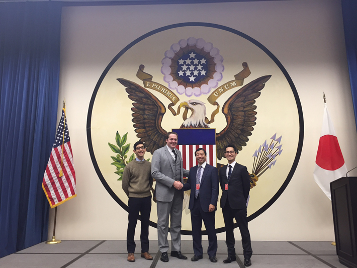 米国大使館にて招待講義後に大使館幹部（左）と記念撮影する井上光太郎教授（左）と池田直史助教（右）