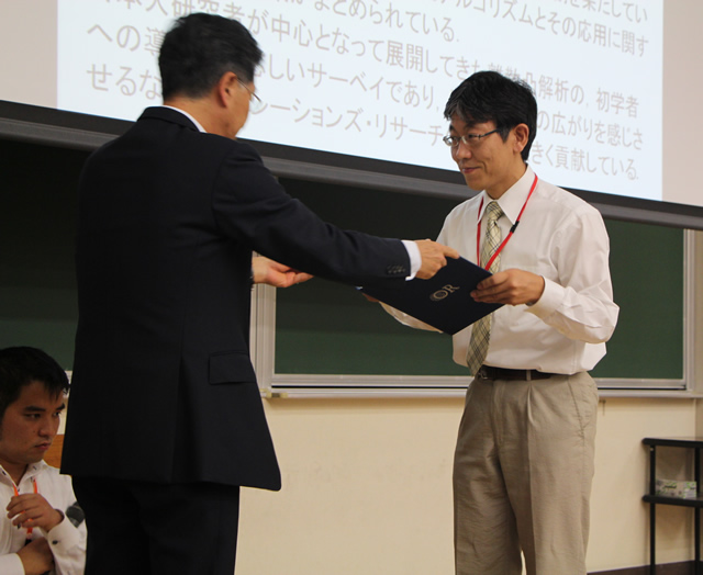 授賞式にて賞状を受け取る塩浦昭義准教授（右）